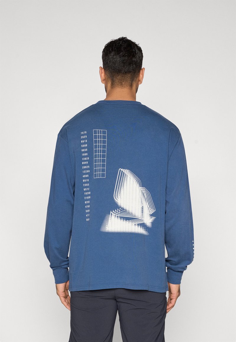 Μπλε πουκάμισο με μακριά μανίκια, με λευκό γεωμετρικό γραφικό και εκτύπωση κειμένου στην πλάτη. Μαλακό ύφασμα, άνετη εφαρμογή, ριμπ μανσέτες και στρογγυλή λαιμόκοψη.