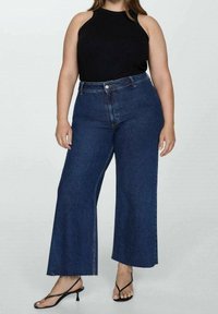 Korkeavyötäröiset tummansiniset leveälahkeiset farkut, joissa on raaka helma, yhdistetty mustaan hihattomaan paitaan ja mustiin remmisandaaleihin.