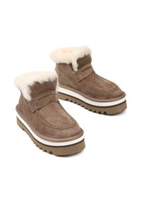 Brązowe zamszowe botki za kostkę z białymi, sztucznymi futrzanymi mankietami, o wzornictwie inspirowanym mokasynami i grubą, ząbkowaną podeszwą z kontrastowym paskiem.