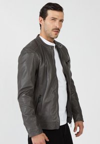 Szara skórzana kurtka ze stójką, z zamkiem błyskawicznym z przodu i prążkowanymi akcentami na ramionach. Posiada dwie boczne kieszenie i gładką teksturę.