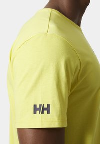 Camiseta amarilla de manga corta, hecha de tela suave. Presenta un logo negro en la manga izquierda y un diseño clásico de cuello redondo.