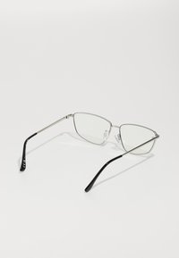 Lunettes avec monture en métal argenté et verres transparents, présentant une forme géométrique et des embouts de branches en plastique noir pour le confort.
