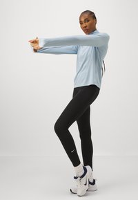 Svijetloplava dugorukava sportska majica s pripijenim crnim tajicama. Kombinacija ima opušteni kroj i Nike logo na tajicama.