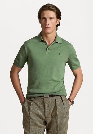 Groene polo met korte mouwen en een kraag, met een subtiele textuur en een klein marineblauw logo op de linkerbovenborst. Gepaard met geruite broek.