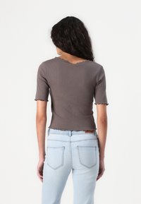 Gray ribbed short-sleeve top with scalloped edges, fitted design, paired with light blue high-waisted jeans with back pockets.