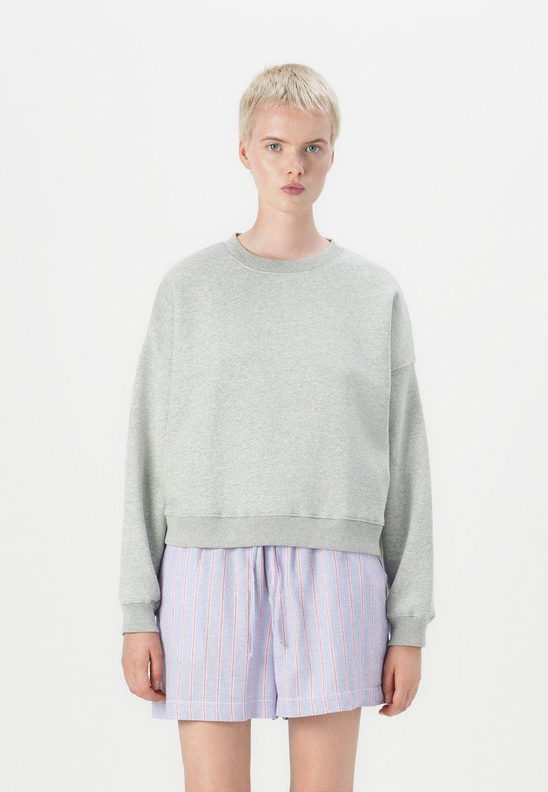 Sweat-shirt gris avec un col rond et des épaules tombantes, associé à un short bleu clair avec des rayures rouges et une taille élastique.