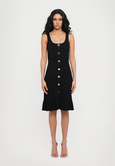 Robe en maille noire avec un décolleté carré, détails en boutons dorés et ourlet évasé. Présente une coupe ajustée et une longueur au genou.