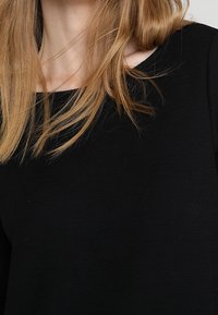 Czarny, prążkowany longsleeve z szerokim dekoltem, ukazujący gładką fakturę materiału i subtelne detale szwów.