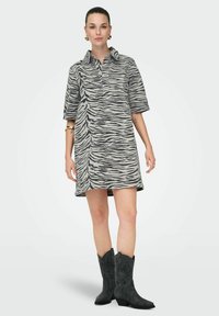 Robe à rayures zèbre en gris et noir, avec un col et des manches courtes. Associée à des bottes de cow-boy grises.