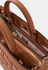 Sac à main en cuir marron avec un design matelassé, une fermeture éclair dorée et deux poignées supérieures. L'intérieur comprend des compartiments et un marquage de la marque.