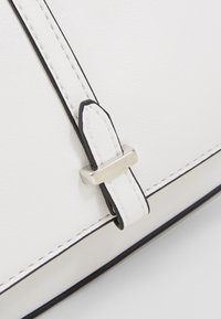Vitt läderhandväska med svart trim, med detaljer i silverfärgad spänne och kontrasterande stygn längs kanten.