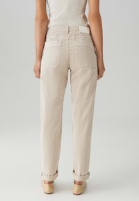 Pantaloni beige a vita alta con vestibilità rilassata, featuring orli arrotolati e due tasche posteriori. Tessuto in cotone liscio con una leggera trama.