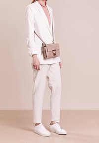 Valkoinen räätälöity bleiseri, vaaleanpunainen toppi, valkoiset housut ja valkoiset tennarit. Pieni beige mokkanahkainen olkalaukku, jossa on kultaiset yksityiskohdat.