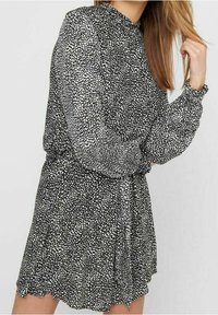 Vestido blanco y negro con un patrón de manchas, mangas largas, escote con volantes y cinturilla con lazo. Tejido ligero con un diseño fluido.