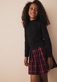 Top negro de manga larga con textura acanalada combinado con falda plisada a cuadros rojos y negros. Tejido suave con diseño ajustado y pliegues definidos.