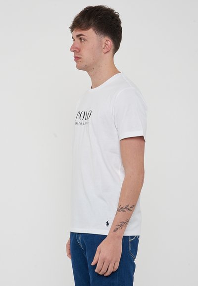 T-shirt bianco in cotone con colletto rotondo e maniche corte. Logo nero "POLO RALPH LAUREN" stampato sul davanti. Piccolo logo di cavallo nero sull'orlo.