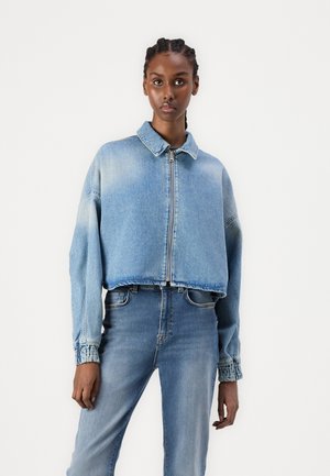 Korte denimmantel in lichtblauw met een ritssluiting, puntkraag en elastische manchetten. Gekleed met bijpassende lichtblauwe jeans.