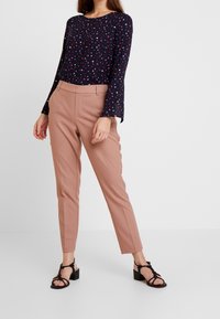 Maglia a maniche lunghe con sfondo blu navy e motivo a triangoli multicolori, abbinata a pantaloni su misura rosa chiaro e sandali neri con tacco a blocco.