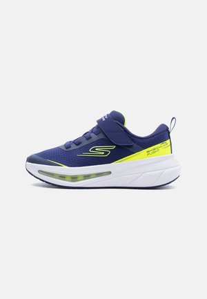 Chaussure de sport Skechers bleu marine et jaune néon avec bride Velcro, tige en mesh et semelle blanche amortie avec coussin d’air visible.