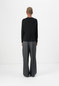 Black long-sleeve top paired with loose-fitting gray trousers. Smooth fabric with a neutral color palette and relaxed silhouette.