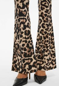 Beige en zwarte stof met luipaardprint, flared broek met een gladde textuur en een scherpe zoom, gecombineerd met puntige zwarte hakken.