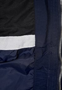 Navy blue jacket interior featuring a textured black lining, a white elastic band, and visible stitching along the edges with a silver zipper.