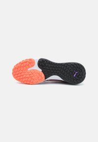 Semelle d'une sneaker avec une base en caoutchouc noir dotée de crampons circulaires, et une section orange vif avec des rainures ovales et un détail de logo violet.