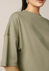 Oversized olivově zelené tričko s žebrovaným kulatým výstřihem a krátkými rukávy, vyrobené z měkké bavlněné směsi. Minimalistický design, bez vzorů.