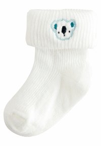 Weiße gerippte Baumwollsocke mit umgeschlagenem Bündchen, auf der Vorderseite mit einem blauen und schwarzen gestickten Bärenkopf verziert. Weiche Textur und runde Zehen.