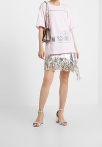 Růžové oversized tričko s potiskem "LOVE MOSCHINO", doplněné stříbrnou sukní s třásněmi z flitrů. Obsahuje malou metalickou kabelku přes rameno. Stříbrné sandály na podpatku.