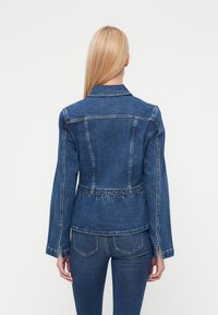 Σκούρο μπλε τζιν μπουφάν με σφηκοφωλιά στη μέση, μακριά μανίκια και κλασικό γιακά. Διαθέτει ραφές σε αντίθεση και λεπτομέρειες με ανοίγματα στα πλάγια.