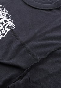 Μαύρο μπλουζάκι από μαλακό ύφασμα, με λευκό σχέδιο στο μπροστινό μέρος. Στρογγυλή λαιμόκο ψη και ορατές ραφές κατά μήκος των ραφών.