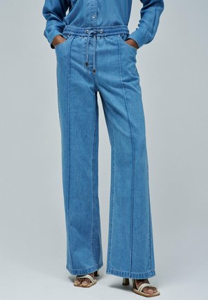 Pantalones de denim de pierna ancha en azul claro con cintura elástica, cierre de cordón y bolsillos frontales. Presenta detalles de costura vertical.