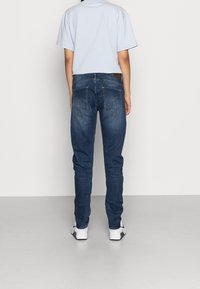 Jeans ajustados de un azul oscuro con una cintura de media altura, que presentan dos bolsillos traseros y sutiles detalles de costura. Combinados con una camiseta corta de un azul claro.