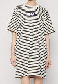Gestreiftes kurzärmliges Kleid in Creme und Marineblau, mit einem runden Halsausschnitt und einem kleinen "GAP"-Logo in Marineblau auf der Brust.