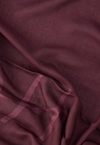 Vīnsarkana caurspīdīga auduma ar mīkstu, viegli teksturētu virsmu, kurā ir smalks režģa raksts gaišākā vīnsarkanā nokrāsā.