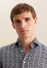 Camicia blu navy con bottoni e motivo floreale bianco, caratterizzata da un colletto classico e da una trama liscia e tessuta.