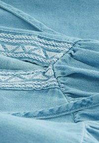 Hele blauw kangas tekstuuri pinnaga, millel on valge tikandmustri äär, kogutud detailidega, et lisada struktuuri.