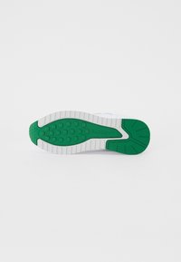 Sole di sneaker bianca con pattern di trazione in gomma verde. Presenta un design testurizzato e un logo di marca sul lato, evidenziando il suo stile atletico.