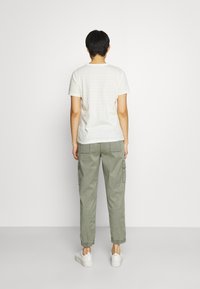 Bílé pruhované tričko, olivově zelené cargo kalhoty s kapsami a bílé tenisky. Jednoduchý design, volný střih a měkká textura.