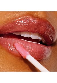 Applicateur de gloss à lèvres avec une pointe douce et effilée appliquant un produit rose transparent et brillant sur des lèvres pleines, révélant une texture lisse et un éclat naturel.