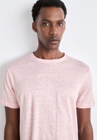 Ljusrosa kortärmad t-shirt i mjukt, texturerat tyg. Har rundad halsringning och något uppvikta ärmslut, med en avslappnad passform.