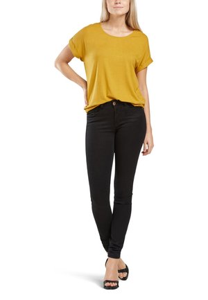 Gul kortærmet top parret med sorte skinny jeans. Toppen er blød og løstsiddende; jeansene er tætsiddende med et klassisk fem-lomme design.