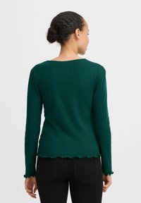 Grünes geripptes Langarmoberteil mit rundem Halsausschnitt und gewelltem Saum. Strukturierter Stoff; taillierte Silhouette; Rückansicht mit Detail der Ärmel.