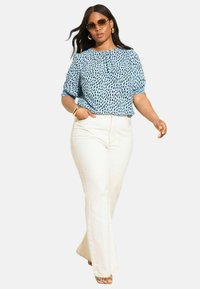 Lysblå bluse med sort prikmønster, elastiske ærmer, parret med højtaljede hvide flarejeans og beige sandaler.