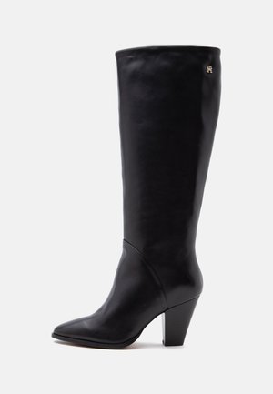 Botte haute en cuir noir pour femme, avec bout pointu, talon bloc et petit logo doré près du haut sur fond neutre.