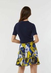 Marineblauw geribbeld T-shirt met korte mouwen, gecombineerd met een knielange rok met een levendig bloemenpatroon in blauw en geel, met een gerimpelde zoom.
