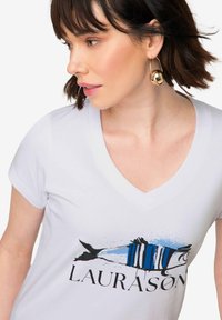Camiseta de algodón blanca con un diseño de escote en V, que presenta un gráfico de pez azul y negro y la palabra "LAURASON" en letras negritas.