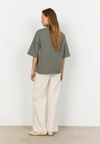 Grå oversized t-shirt med korte ærmer, parret med cremefarvede bukser med brede ben. Glat tekstur, minimalisk design og subtile detaljerne i kanten.
