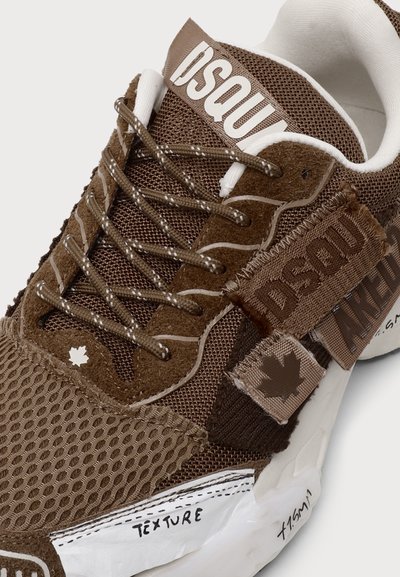 Κοντινή λήψη ενός καφέ sneaker από δίχτυ και σουέντ με κορδόνια, λευκή σόλα, λογότυπο "DSQU", εικονίδιο φύλλου σφενδάμου και υφασμάτινες λεπτομέρειες με υφή.